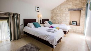 Habitación de hotel con dos camas, una pared de piedra, una ventana con cortinas y un pequeño estante con fotografías.