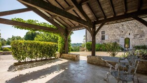 Un espacio de patio exterior con piso de piedra, una estructura de pérgola y un edificio de piedra al fondo.