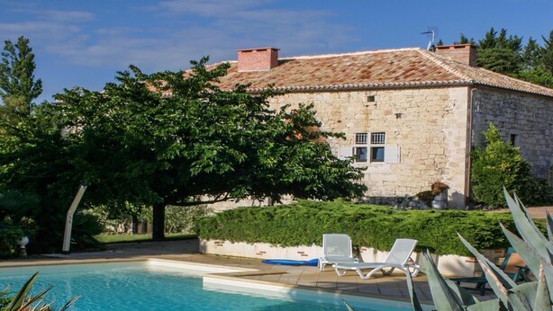 Un edificio de piedra con techo de tejas, piscina y sillas de descanso.