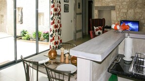 A dining area with a table set for two, a stone wall, a television, and a window with a curtain. - Gîte with swimming pool and park garden (Saint Maurin)