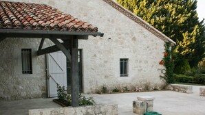 A stone building with a tiled roof, a covered porch, and a garden area with a hose. - Gîte with swimming pool and park garden (Saint Maurin)