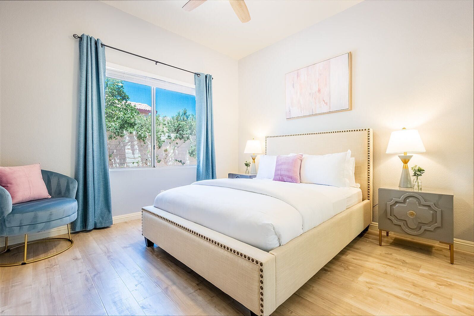 A bedroom with a large bed, a chair, a nightstand, a lamp, and a window with curtains.