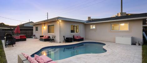 A backyard with a swimming pool, outdoor seating, and a house.