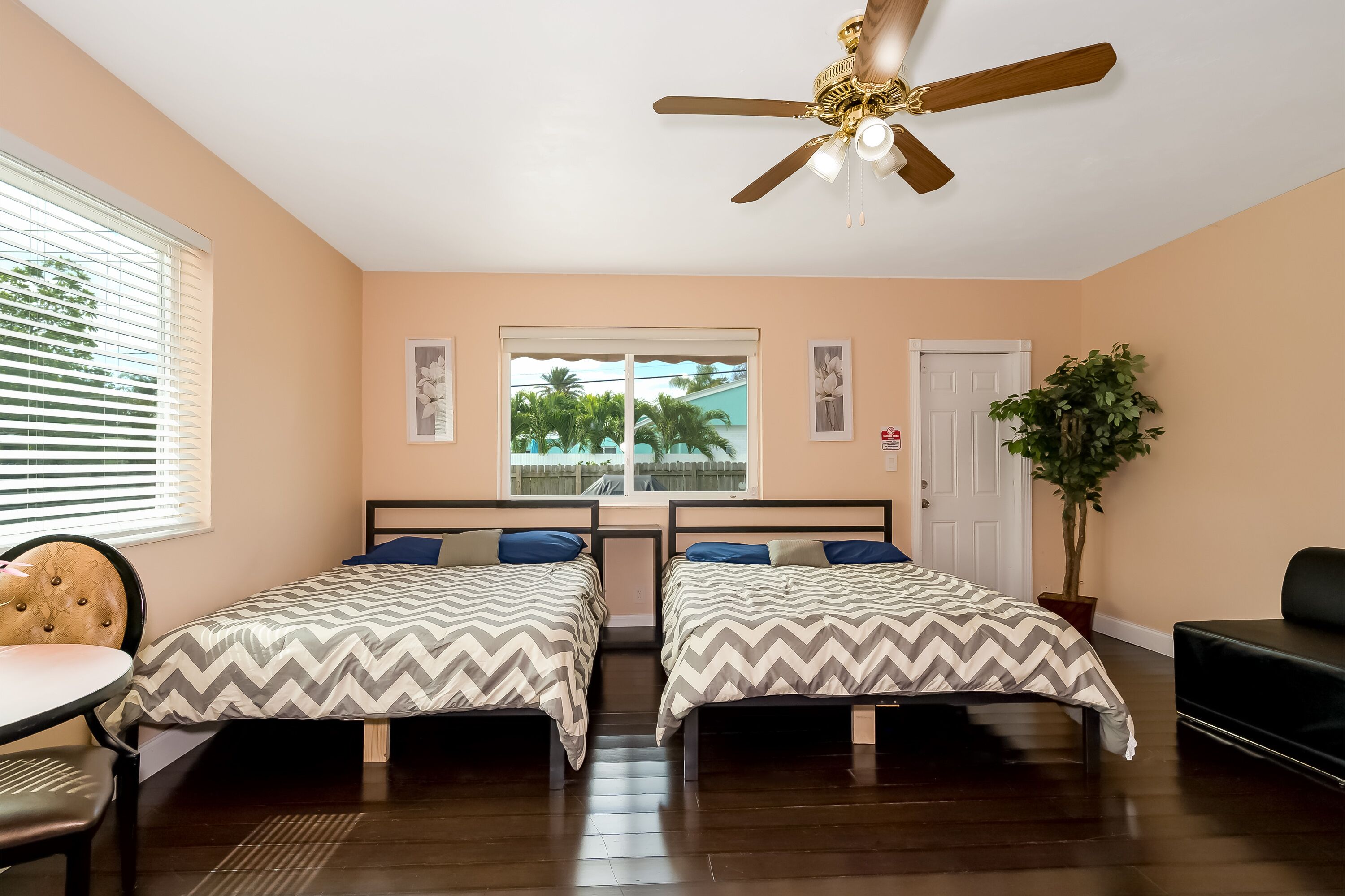 A bedroom with two beds, a ceiling fan, a window with a view, and a potted plant.