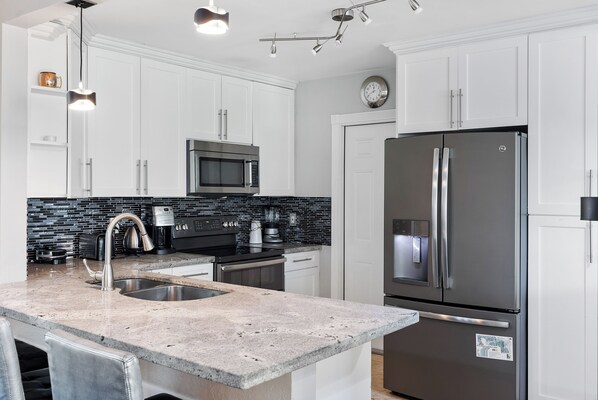 A modern kitchen with white cabinets, a stainless steel refrigerator, a black microwave, and a granite countertop.
