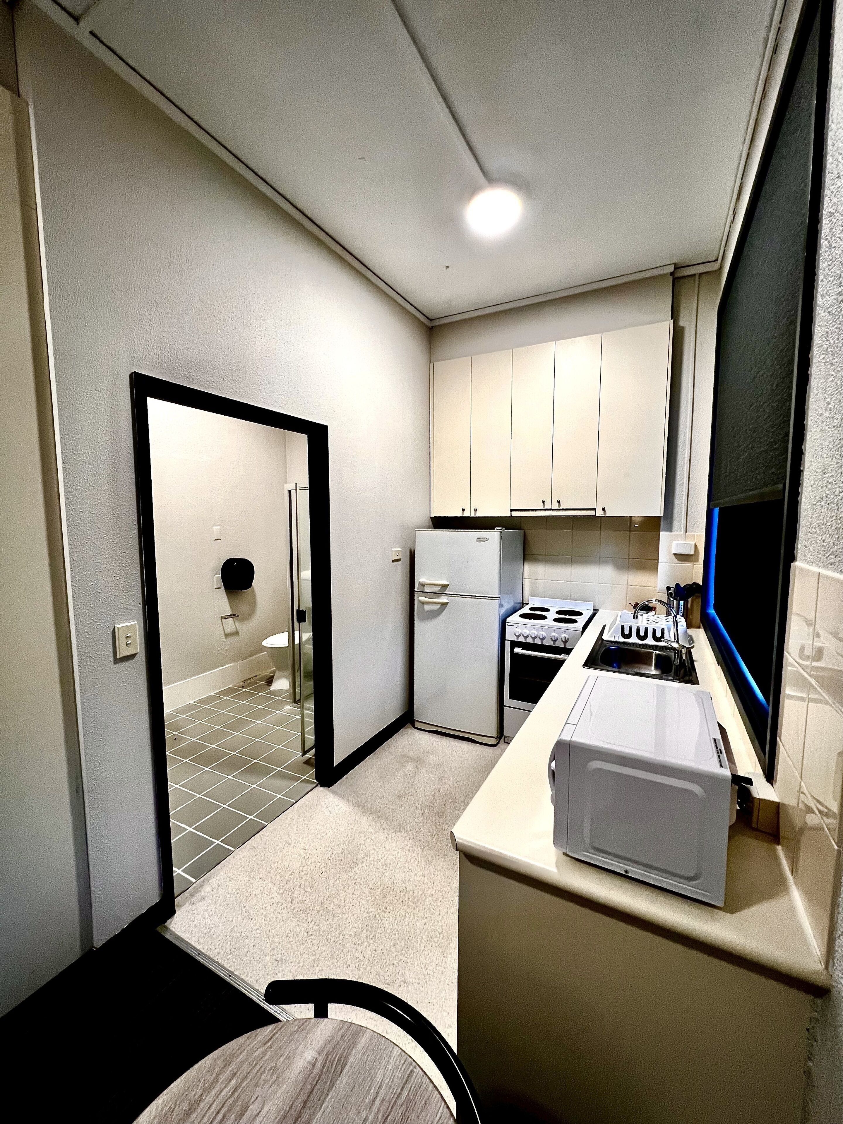 A compact kitchen with white cabinets, a refrigerator, a stove, and a microwave.