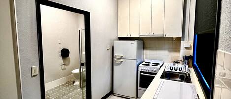 A compact kitchen with white cabinets, a refrigerator, a stove, and a microwave.