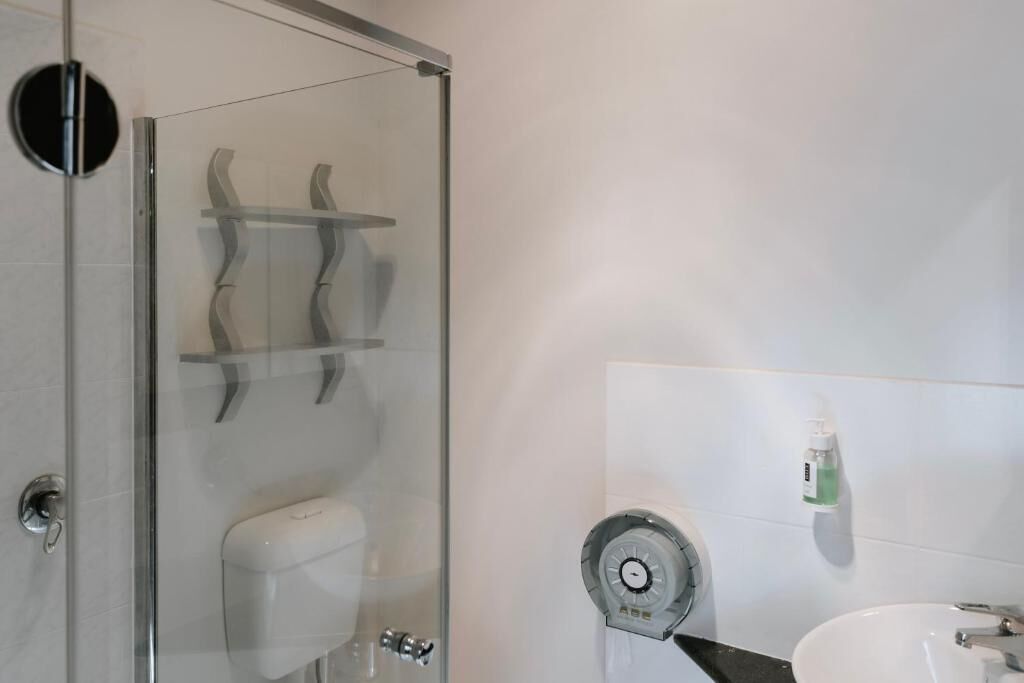 Une salle de bain moderne avec une douche à parois de verre, des toilettes et un lavabo équipé d’un distributeur de savon.