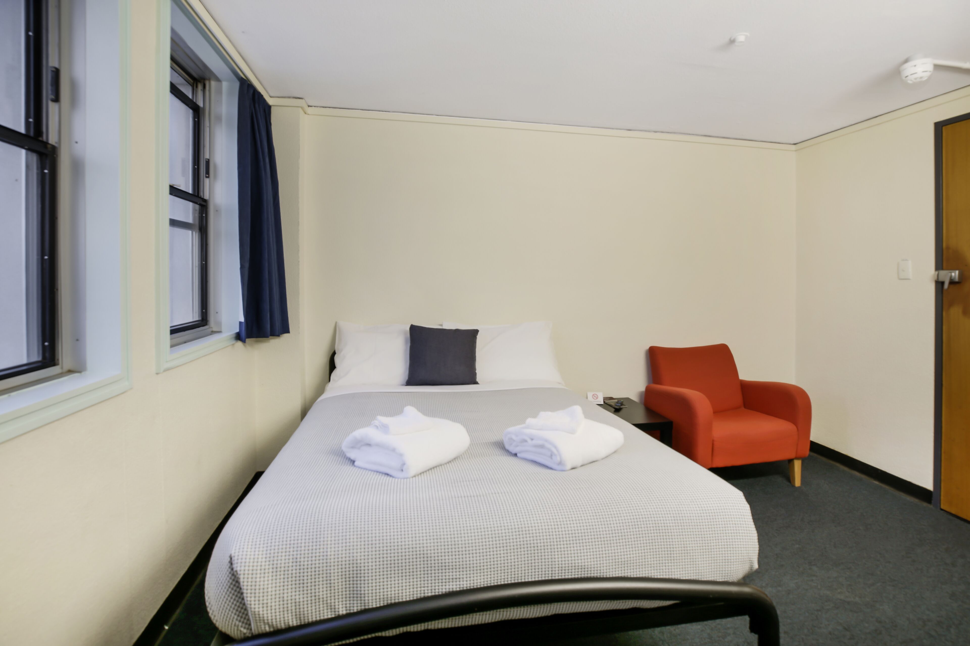 Una habitación de hotel con una cama, una silla y un ventanal con cortinas.