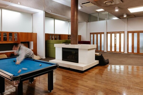 Un espacio interior moderno con mesa de billar, chimenea y zona de estar con un sofá verde.