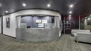 A reception area with a curved desk, a grey sofa, and a glass partition. - Canberra Accommodation Centre (Braddon)