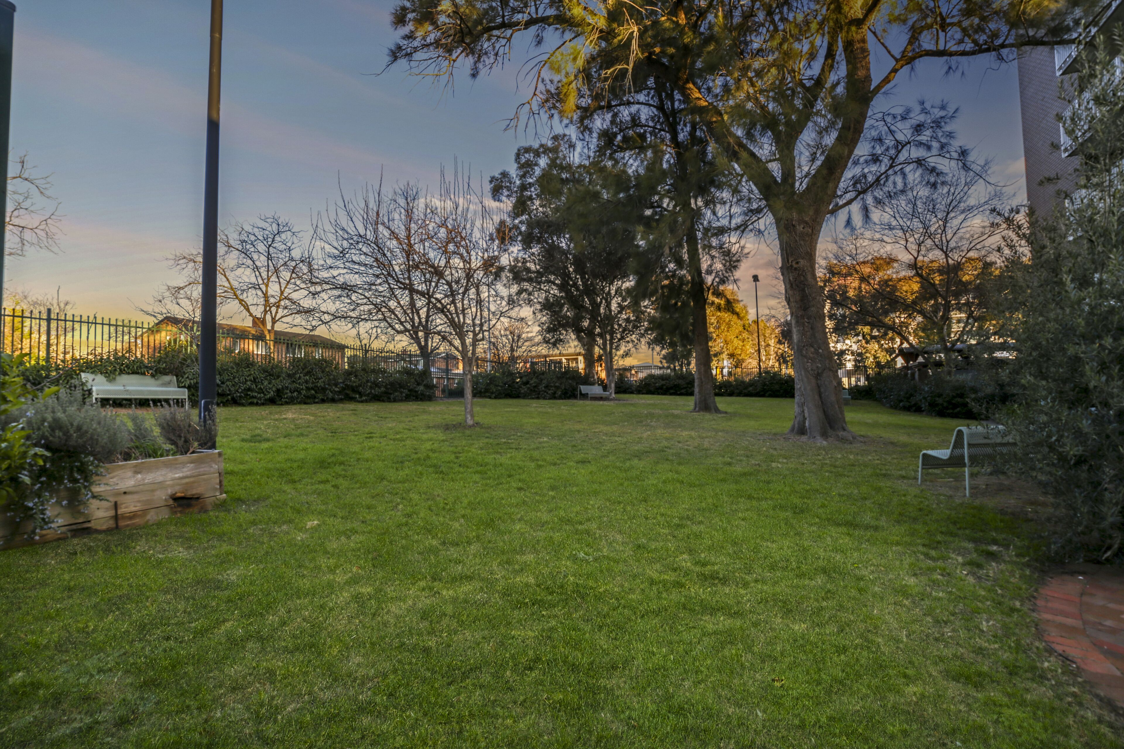 A grassy park area with benches and trees.