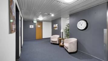 A hallway with grey walls, a clock, two chairs, and a small table with a lamp.