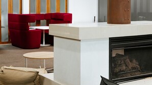 A modern lounge area with a fireplace, red seating, and a white counter. - Canberra Accommodation Centre (Braddon)