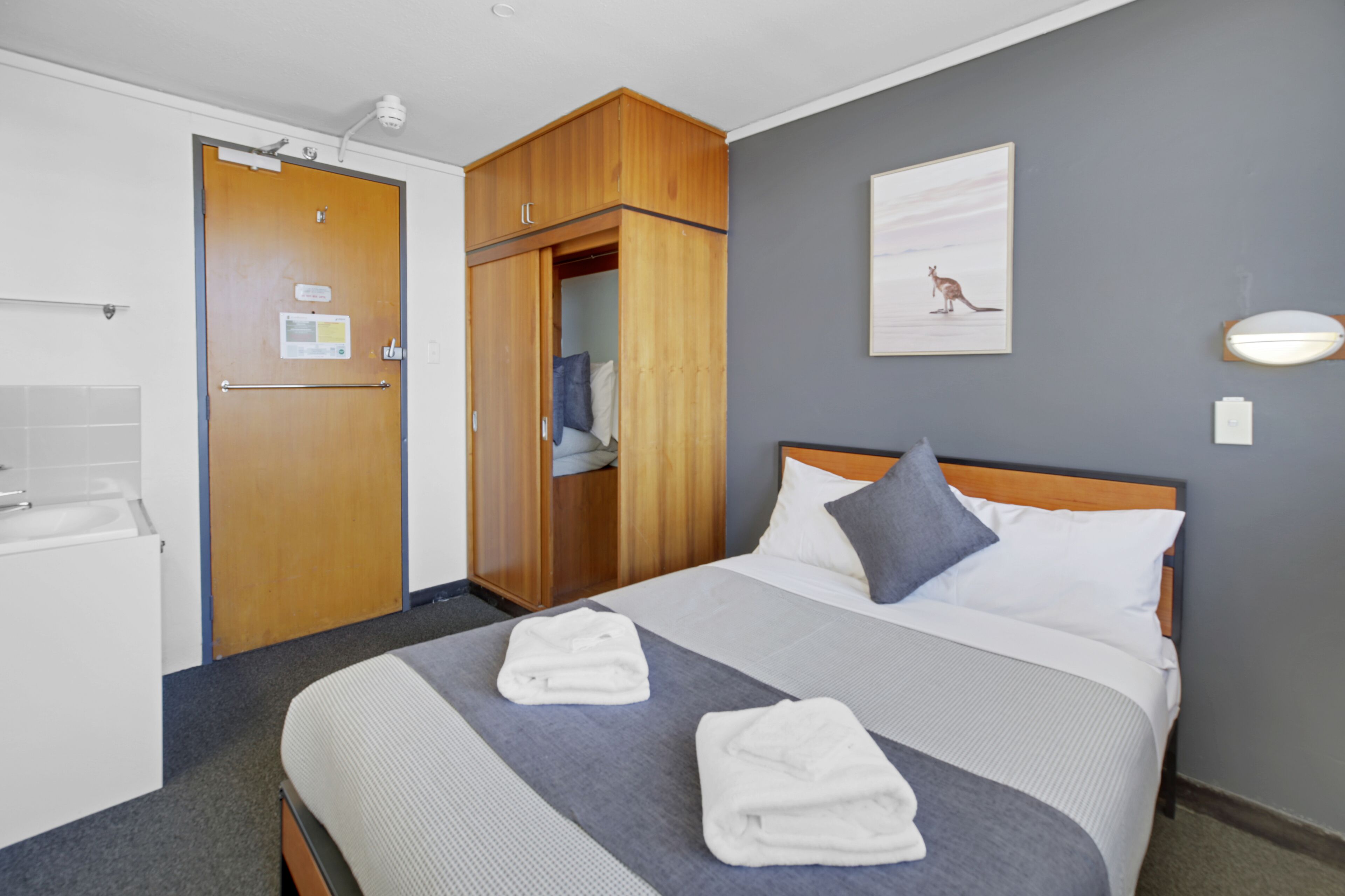 Une chambre d’hôtel comprenant un lit, une armoire, une salle de bain et un luminaire fixé au mur.