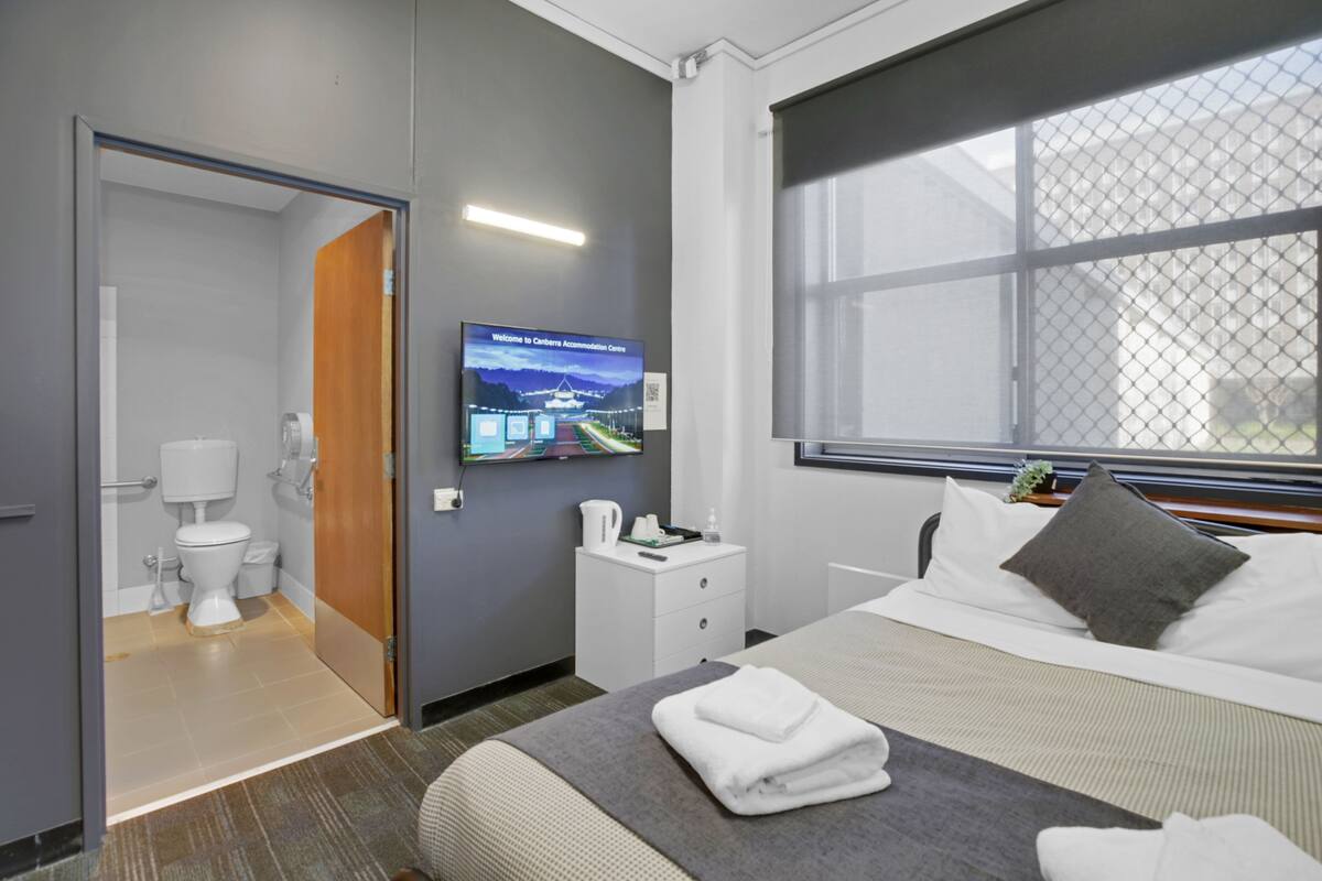 Ein Hotelzimmer mit Bett, Fernseher an der Wand, Fenster mit Blick, Nachttisch und Badezimmer mit Toilette und Waschbecken.
