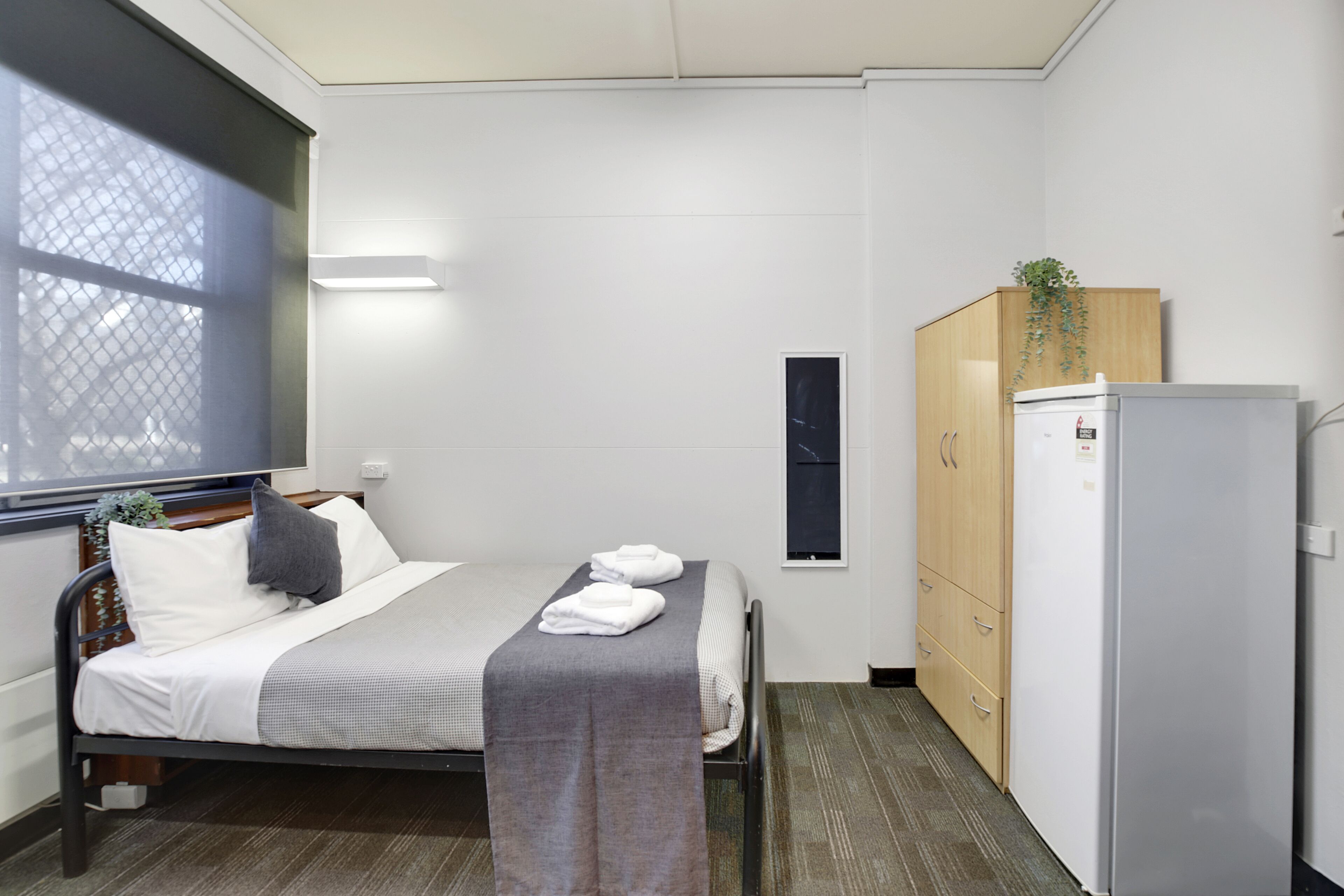 Ein kleines, ordentlich eingerichtetes Schlafzimmer mit einem Bett, einem Kleiderschrank und einem Kühlschrank.