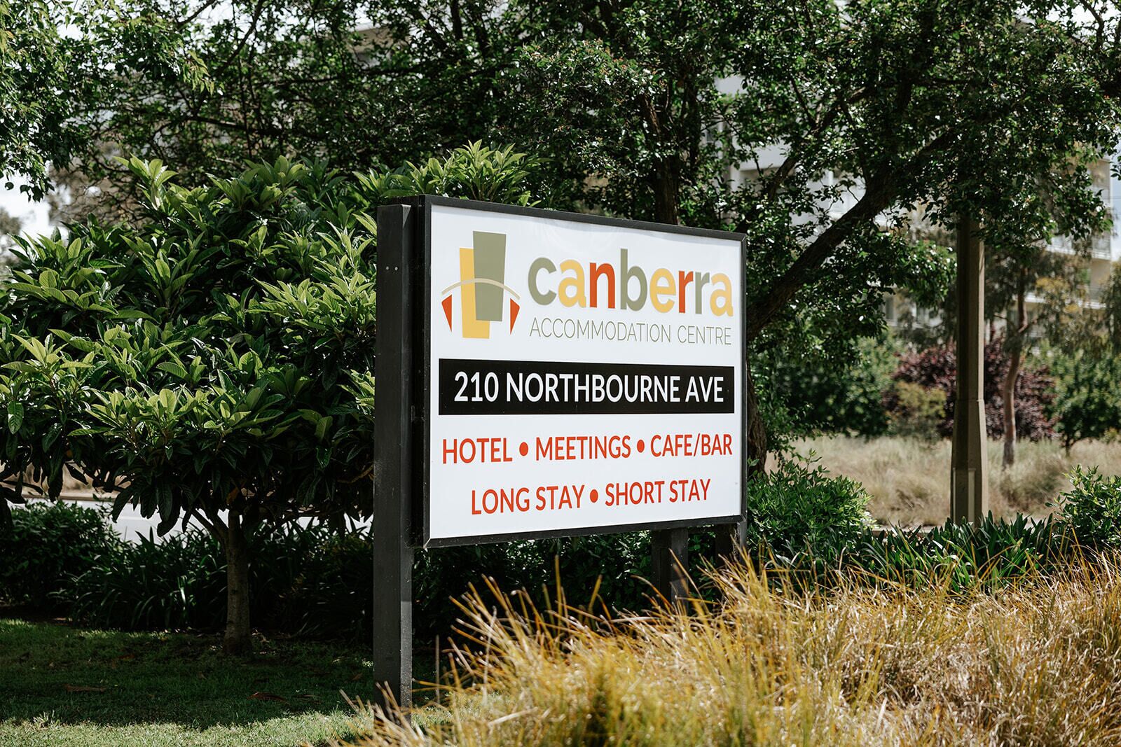 A sign for the Canberra Accommodation Centre at 210 Northbourne Ave, listing amenities like hotel, meetings, cafe/bar, and options for long stay or short stay.