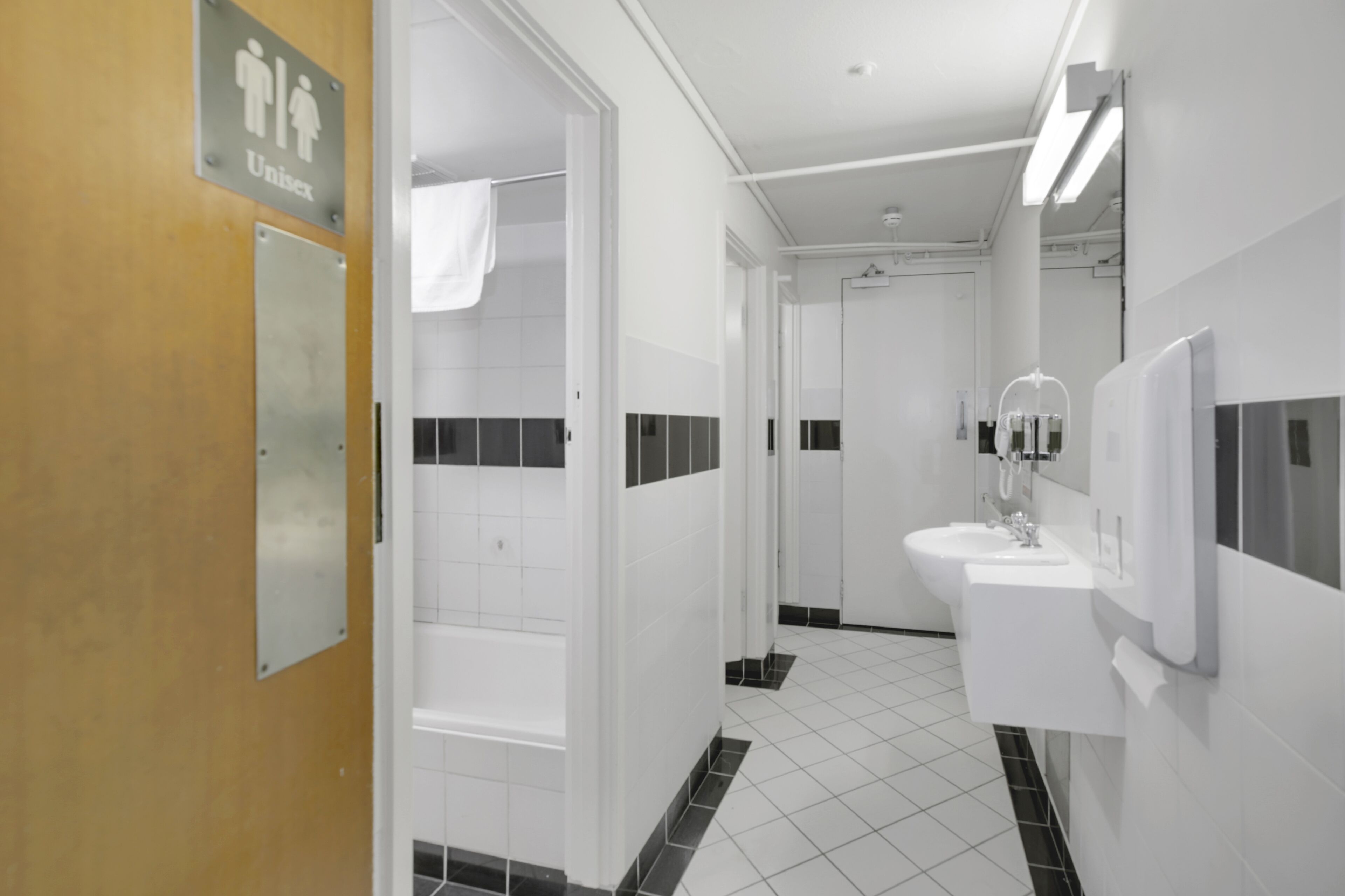 Une salle de bain moderne avec un carrelage noir et blanc, un lavabo, un miroir et un panneau indiquant des toilettes mixtes.