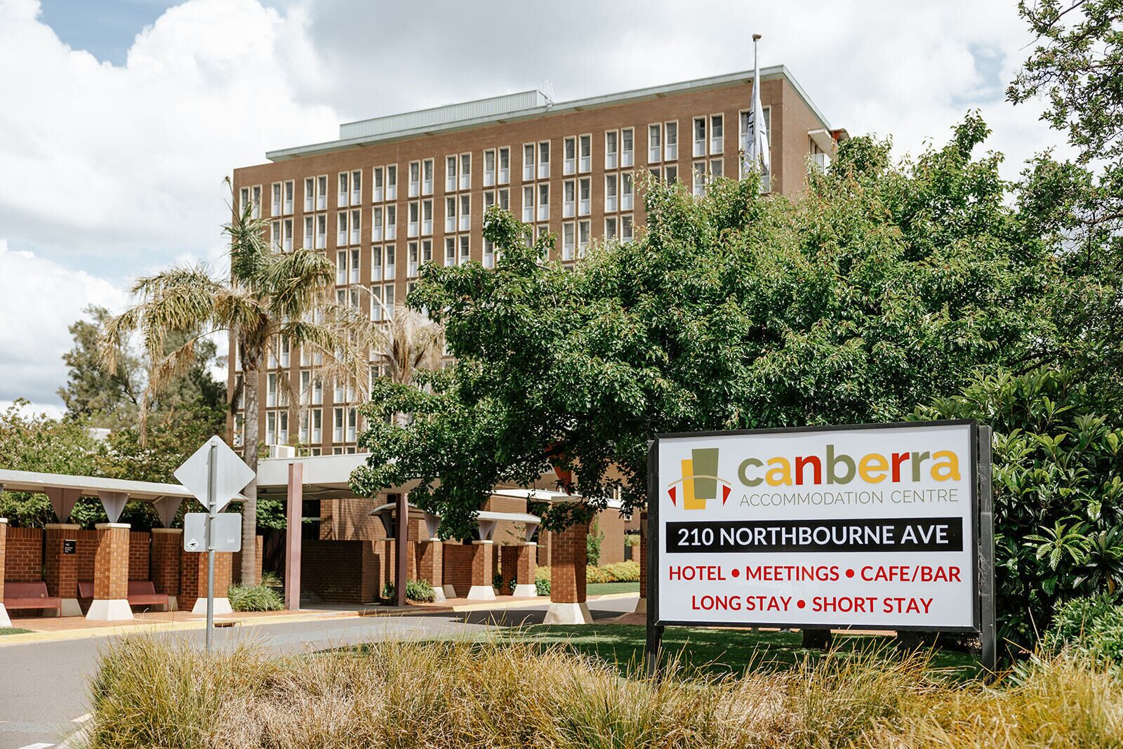 Señal del Canberra Accommodation Centre en el 210 de Northbourne Ave, que indica que ofrece servicios de hotel, salas de reuniones, cafetería/bar, estadías prolongadas y estadías cortas.