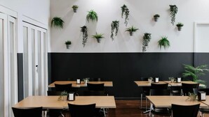 A modern meeting room with wooden tables and black chairs, featuring hanging plants on the walls. - Canberra Accommodation Centre (Braddon)