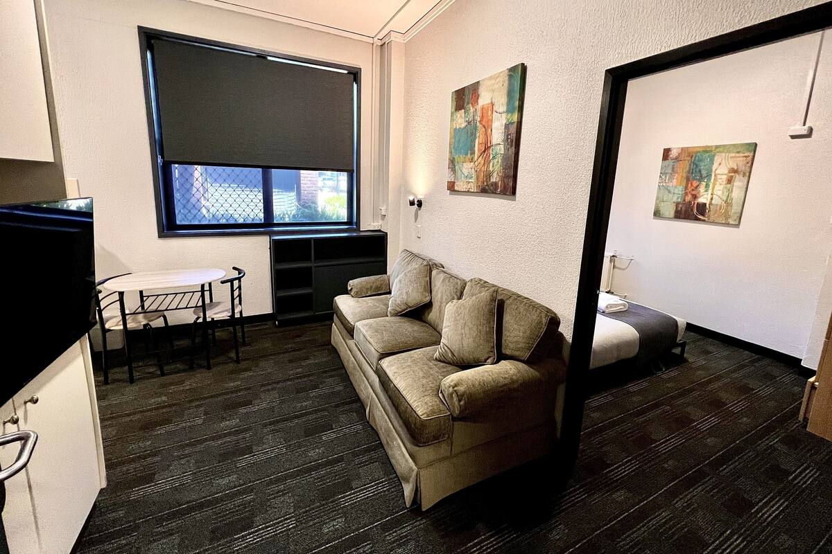 Ein kompakter Wohnraum mit einer Couch, einem kleinen Tisch und einem Fenster mit Jalousien.