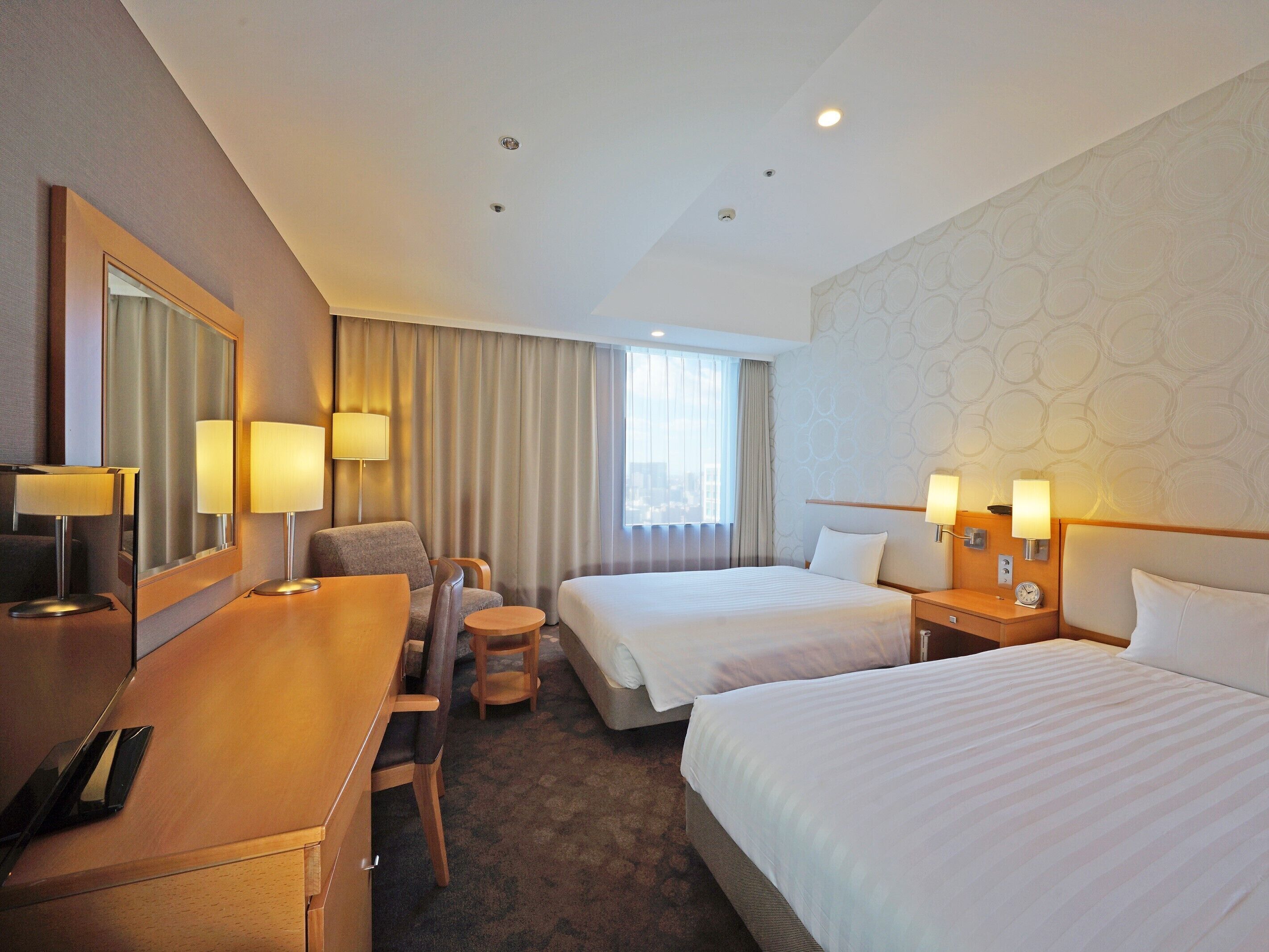 A hotel room with two beds, a desk, a chair, a mirror, and two bedside tables with lamps.
