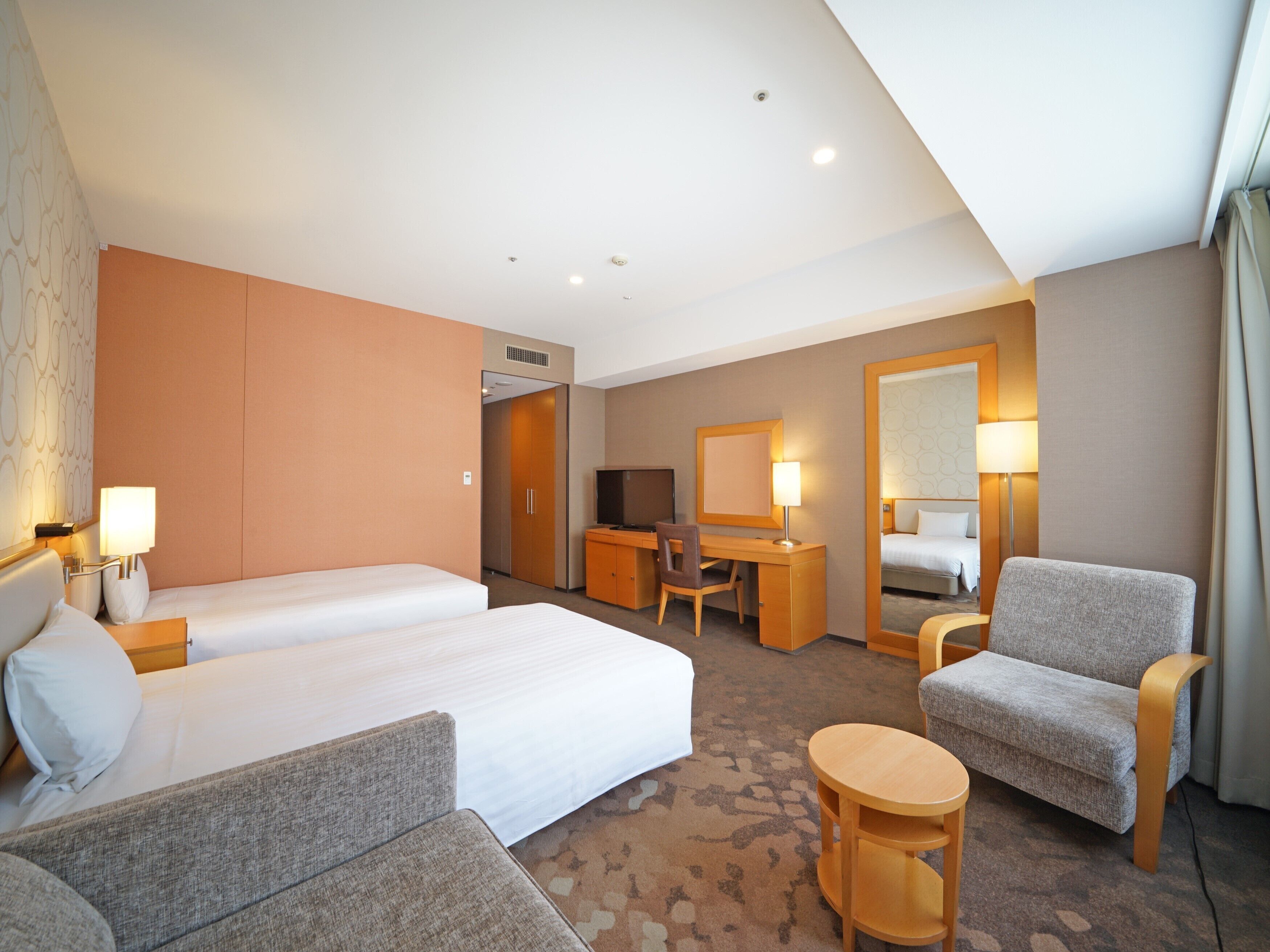 A hotel room with two beds, a desk, a chair, a small table, and a mirror.