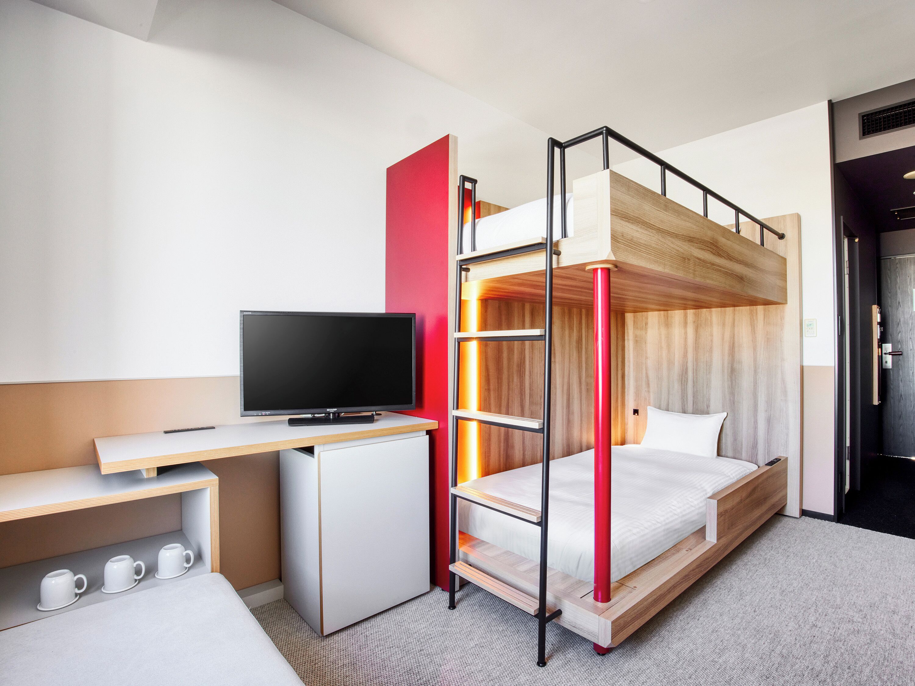 A compact hotel room with a bunk bed, a desk with a television, and a small refrigerator.