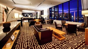 A modern hotel lobby with a geometric patterned carpet, a reception desk, seating area with sofas and chairs, and large windows offering a city view. - LOISIR HOTEL SHINAGAWA SEASIDE (Tokyo)