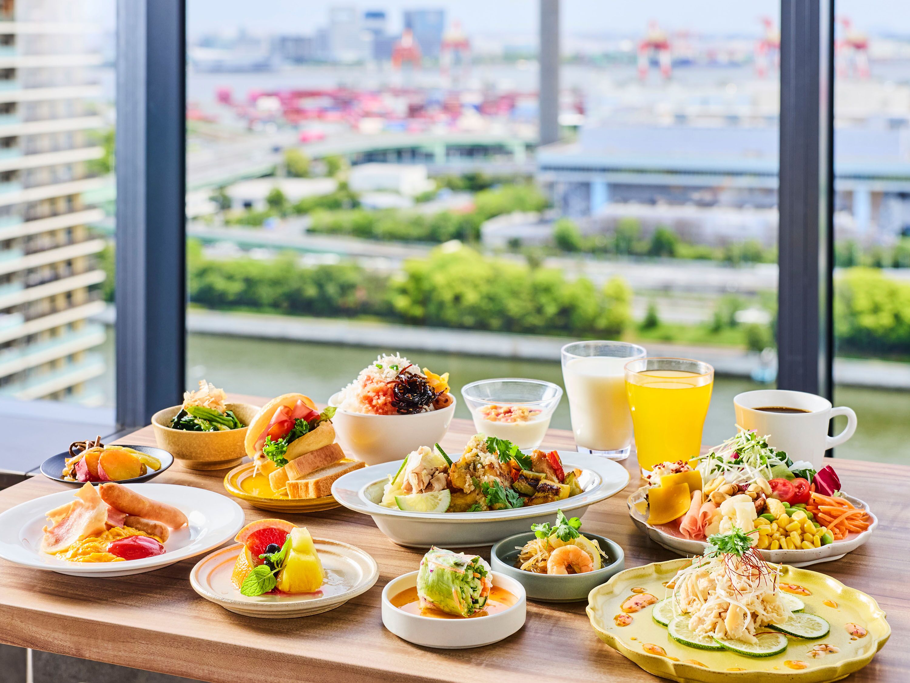 A table with various dishes and drinks, a window with a view of a cityscape.