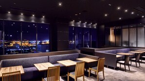 A modern restaurant with high tables and benches, large windows offering city views, and a dark interior with star-shaped ceiling lights. - LOISIR HOTEL SHINAGAWA SEASIDE (Tokyo)
