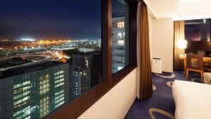 A hotel room with a large window overlooking a cityscape at night, featuring modern buildings and a highway. - LOISIR HOTEL SHINAGAWA SEASIDE (Tokyo)