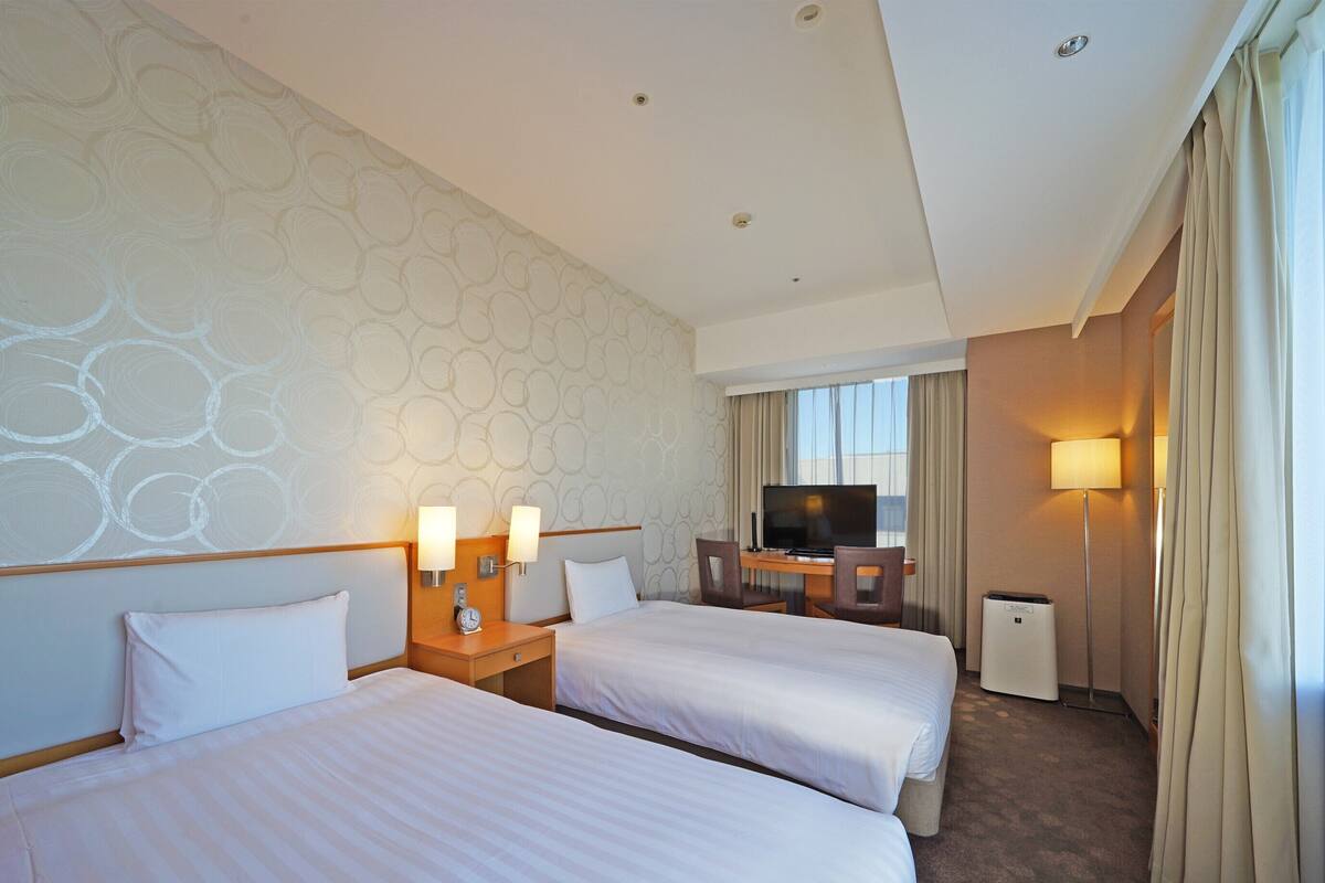 A hotel room with two beds, a TV, a desk, and a lamp.