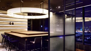A modern bar area with a wooden counter, bar stools, and a large illuminated light fixture. - LOISIR HOTEL SHINAGAWA SEASIDE (Tokyo)