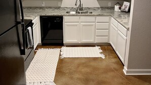 Cozinha com armários brancos, geladeira preta, bancada de granito, pia e backsplash com canecas.