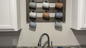 Cozinha com bancada de granito, pia de aço inoxidável e um suporte de madeira com seis canecas.
