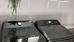 Uma lavanderia moderna com duas máquinas de lavar e secar de aço inoxidável, um aviso de lavanderia automática e uma planta pendurada.