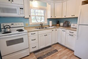 A kitchen with white cabinets, a stove, a microwave, a sink, and a window.