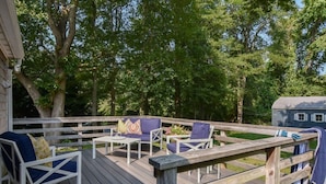 A wooden deck with outdoor furniture, including chairs and a table, surrounded by trees. - Outdoor Oasis w Fire Pit, Hammock, 1 Mi to Beach! (Brewster)