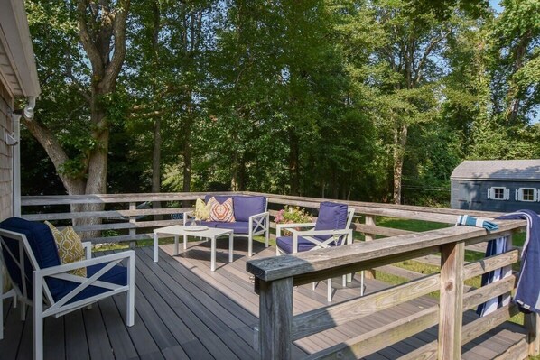 Eine Holzterrasse mit Gartenmöbeln, darunter Stühle und ein Tisch, umgeben von Bäumen.