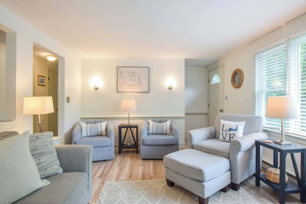 A living room with a sofa, two armchairs, a coffee table, and a rug. There are two wall-mounted lamps, a framed map, and a mirror on the wall.