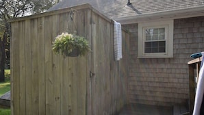 A wooden shed with a hanging planter, adjacent to a house with a window and a door. - Outdoor Oasis w Fire Pit, Hammock, 1 Mi to Beach! (Brewster)