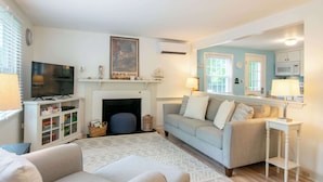 A living room with a fireplace, a television, a sofa, and a small table. - Outdoor Oasis w Fire Pit, Hammock, 1 Mi to Beach! (Brewster)