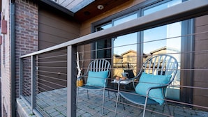 Un balcon avec deux chaises et une petite table, une rambarde en métal et une vue sur un immeuble en briques.