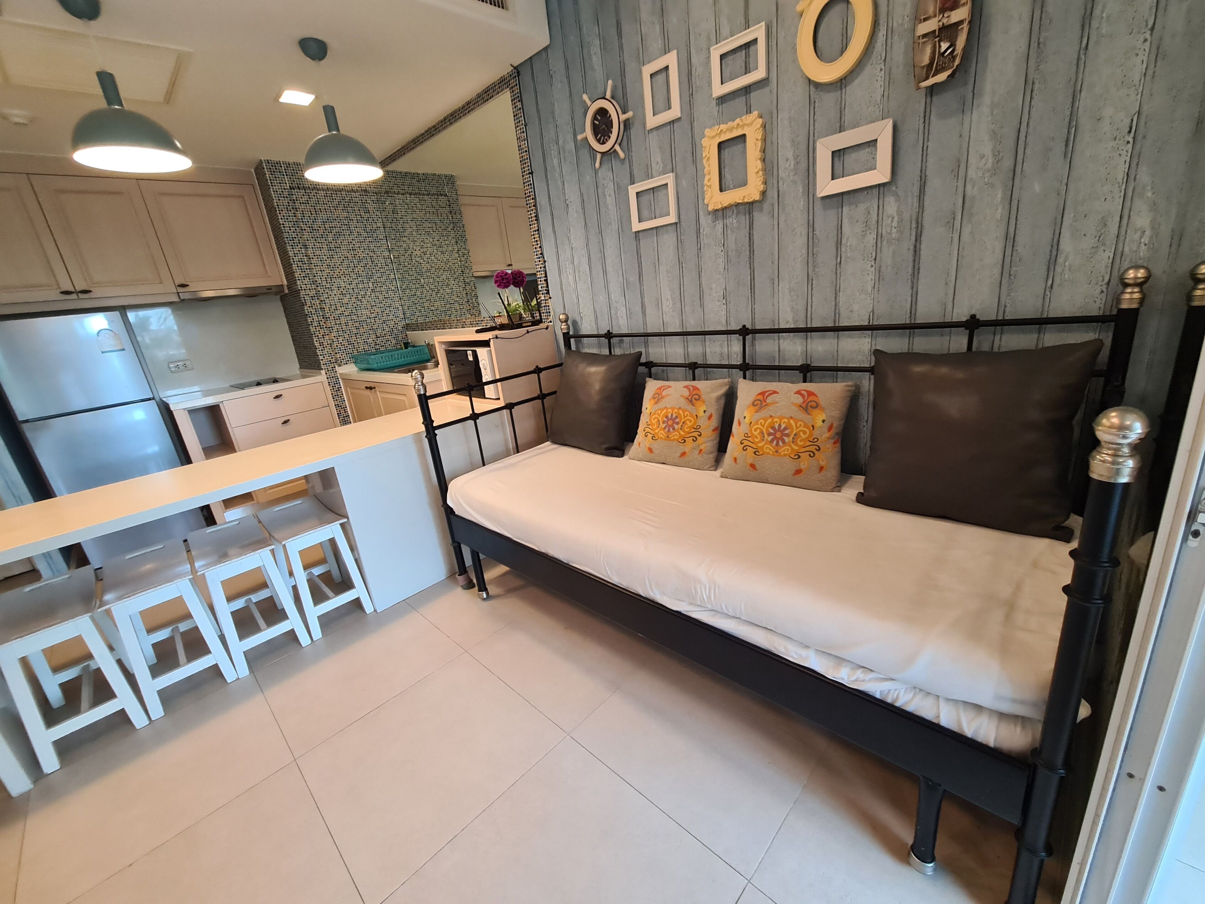 A compact living space with a kitchenette, a bed with decorative pillows, and a wall adorned with framed pictures.