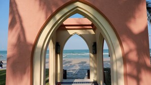 Vista da praia através de uma estrutura com arcos, que dá para uma praia de areia e oceano.