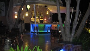 Espaço de bar ao ar livre com piscina, espreguiçadeiras e balcão de bar com painel iluminado e colorido.