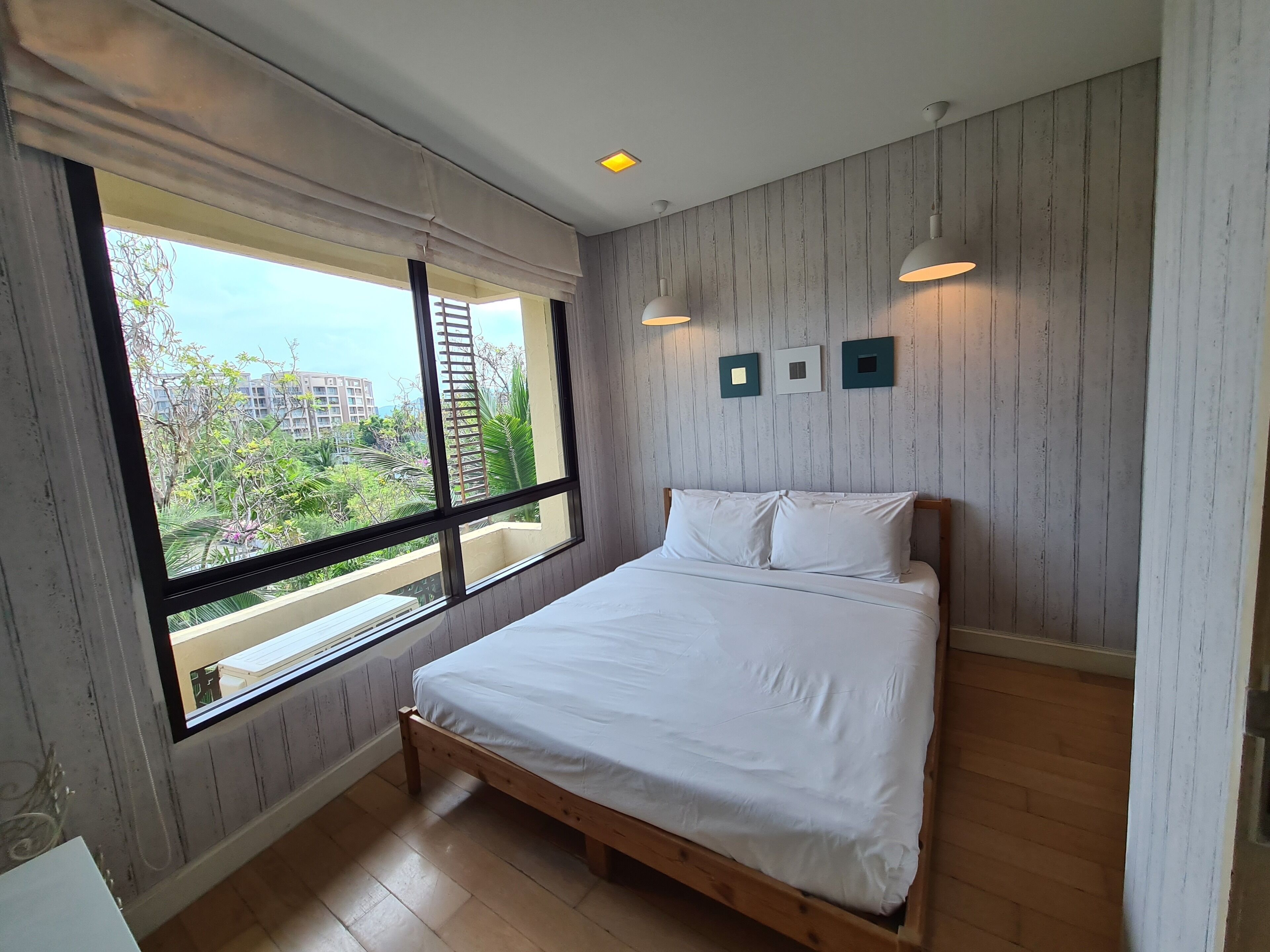 A bedroom with a large window, wooden floor, and a bed with white bedding.