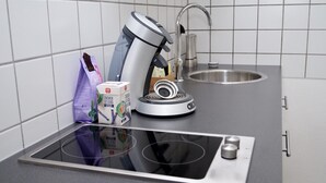 Eine Küche mit integriertem Induktionskochfeld, einer Kaffeemaschine und einer Packung Kaffee-Kapseln.
